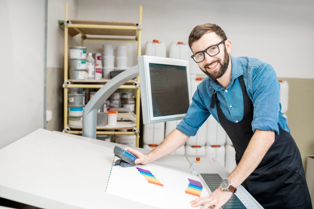 Man worker measuring printing color with spectrometer on the operating desk of the printing plant